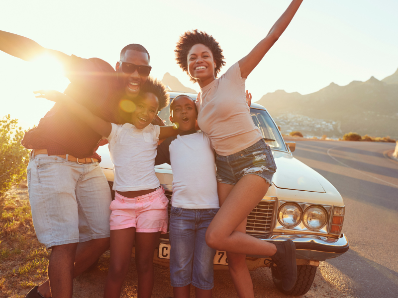 Planning A Road Trip - Family posing in front of car on side of road